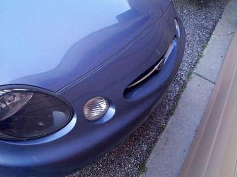 1999 Ford Taurus - The front corner of a blue car shows its headlight and fog light assembly, with a hint of the grille.