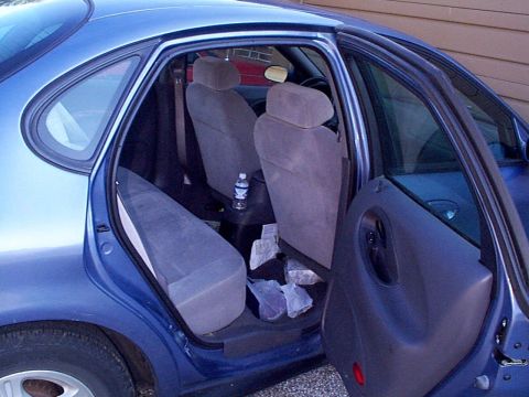 1999 Ford Taurus - The interior of a blue sedan, showing the back seats and open doors, with a water bottle visible.