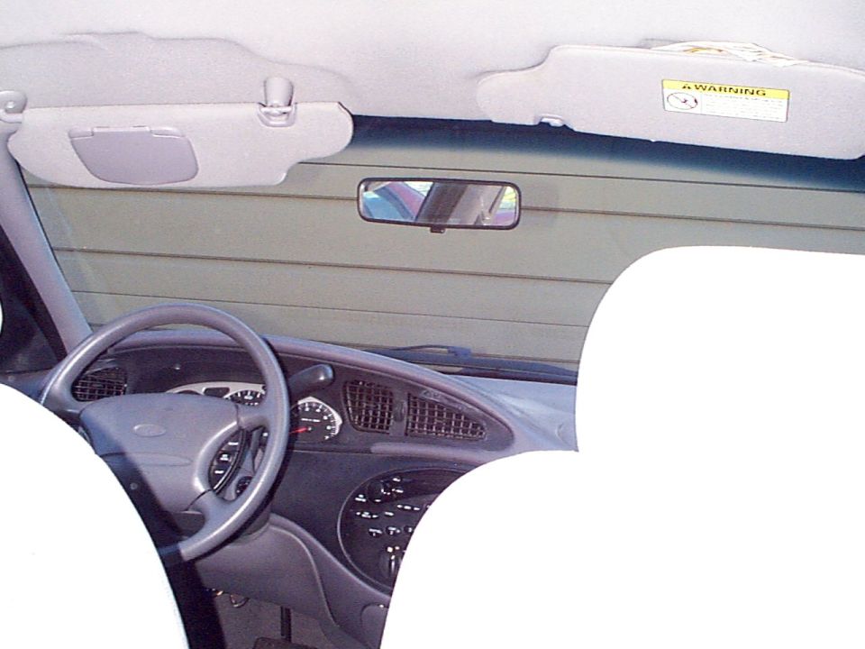 1999 Ford Taurus interior showing dashboard, steering wheel, and sun visors. Warning label visible on passenger sun visor