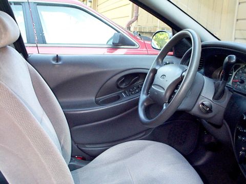 1999 Ford Taurus - Interior view of a 1999 Ford Taurus, showing the driver's side door panel, steering wheel, and dashboard. Another vehicle is visible throug…