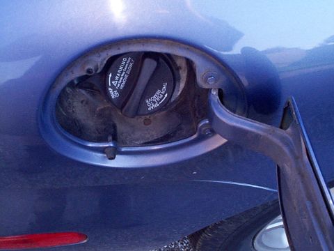 1999 Ford Taurus - Close-up of a blue car's fuel door, showing the gas cap with warning instructions.