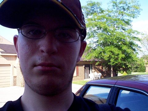 1999 Ford Taurus - A person takes a selfie with a maroon car parked in front of a house and a large tree.