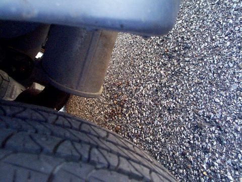 1999 Ford Taurus - A close-up view shows a vehicle's exhaust system and tire against a gravel background.