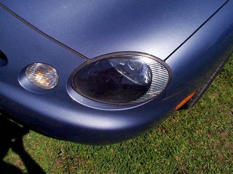 1999 Ford Taurus - Close-up of the front corner of a blue 1999 Ford Taurus, showing the headlight and turn signal assembly.