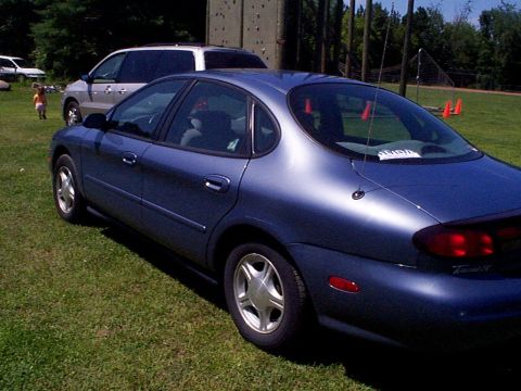 1999 Ford Taurus - A blue 1999 Ford Taurus sedan is parked on a grassy field next to a minivan.