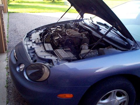 1999 Ford Taurus - The engine bay of a blue 1999 Ford Taurus is visible with the hood open.
