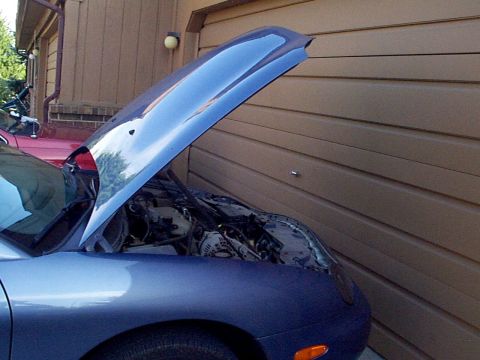1999 Ford Taurus - Engine compartment of a blue car, with another vehicle partially visible in the background.