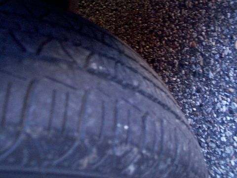 1999 Ford Taurus - The tread of a tire is shown in close-up, with a gravel surface in the background and a website logo at the bottom.