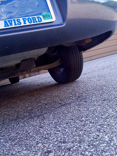 1999 Ford Taurus - The rear wheel and undercarriage of a 1999 Ford Taurus are visible, with a license plate that reads AVIS FORD NOV.