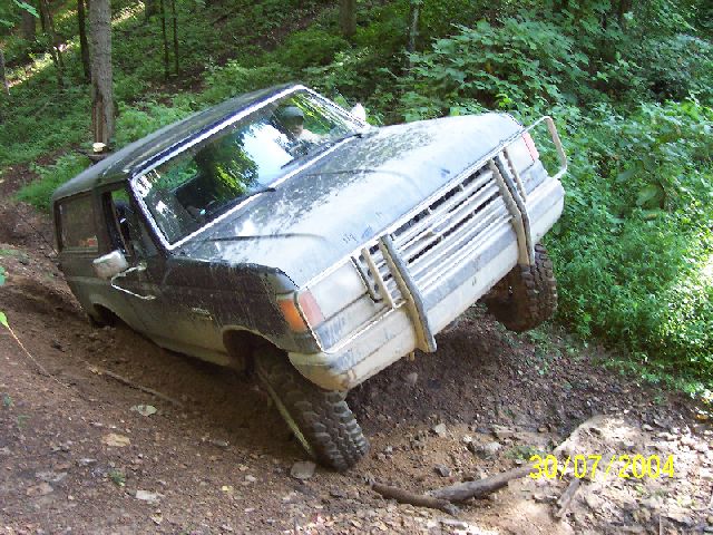 Dark blue Ford Bronco tilted on a muddy incline, front grille guard visible