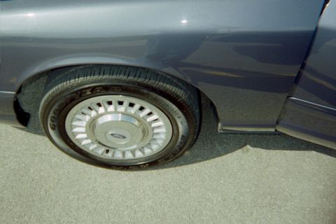 1998 Ford Crown Victoria - A close-up shows the rear wheel and part of the fender of a car, with a Ford logo visible on the hubcap.