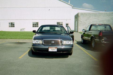 1998 Ford Crown Victoria - A dark blue 1998 Ford Crown Victoria is parked in a lot next to a pickup truck, with its driver's side door ajar.