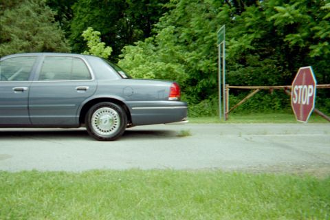 1998 Ford Crown Victoria - A gray Ford Crown Victoria is parked near a stop sign and a wooden gate.