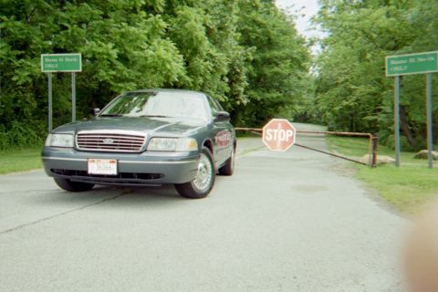 1998 Ford Crown Victoria - A 1998 Ford Crown Victoria approaches a closed gate with stop signs and route markers.