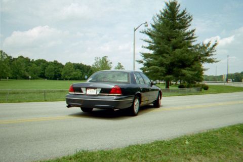 1998 Ford Crown Victoria - A dark blue 1998 Ford Crown Victoria sedan is seen from the rear driving on a road with a yellow line.