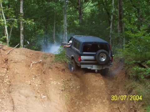 1995 Ford Bronco - 1995 Ford Bronco navigates a steep, wooded trail, kicking up dust and smoke.