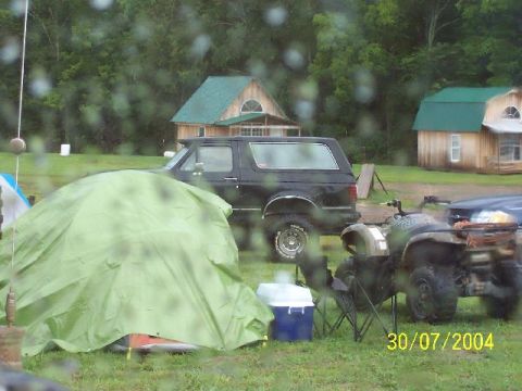 1995 Ford Bronco - A black SUV and an ATV are parked in a grassy area with tents and buildings visible.