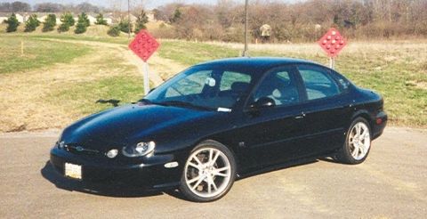 1999 Ford Taurus - A black 1999 Ford Taurus sedan is parked outdoors with a grassy area and trees in the background.