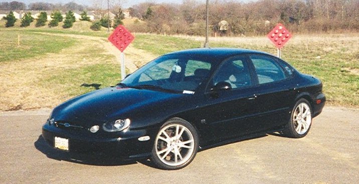 Black 1999 Ford Taurus sedan parked on asphalt, 3/4 front view, showing alloy wheels and tinted windows