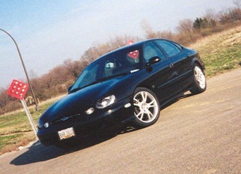 1999 Ford Taurus - Black 1999 Ford Taurus sedan with aftermarket wheels on a sunny day.