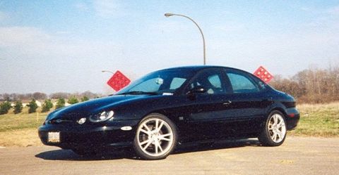 1999 Ford Taurus - A black sedan is parked on the side of the road with a clear sky above.