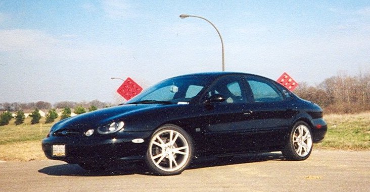 Dark Ford Taurus sedan in profile, lowered on multi-spoke alloy wheels