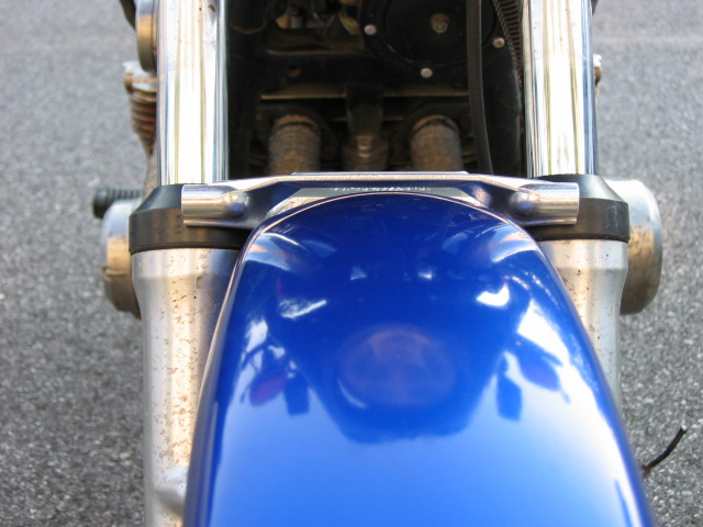 Blue motorcycle front fender and chrome forks with visible engine components behind