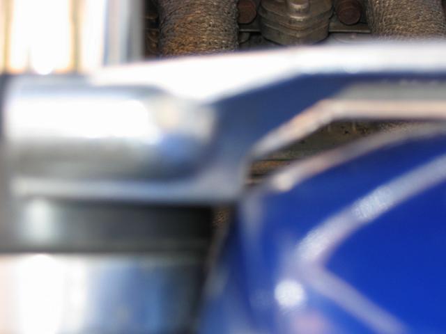 Close-up of a blue engine component with metal tubing and other engine parts in the background