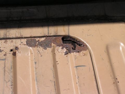 1985 Ford Bronco - Detail of a rusted metal panel with a hook attachment, likely from a vehicle part.