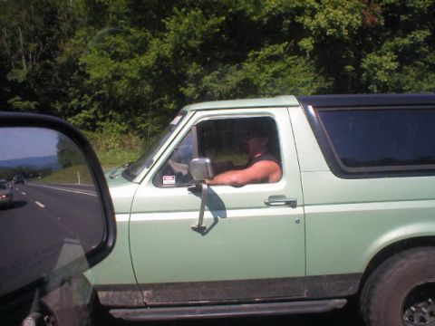 1989 Ford Bronco - A man drives a light green SUV on a highway, viewed from another vehicle.