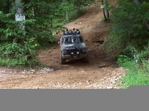 1995 Ford Bronco - This SUV is navigating a steep, rocky, and wooded off-road trail.