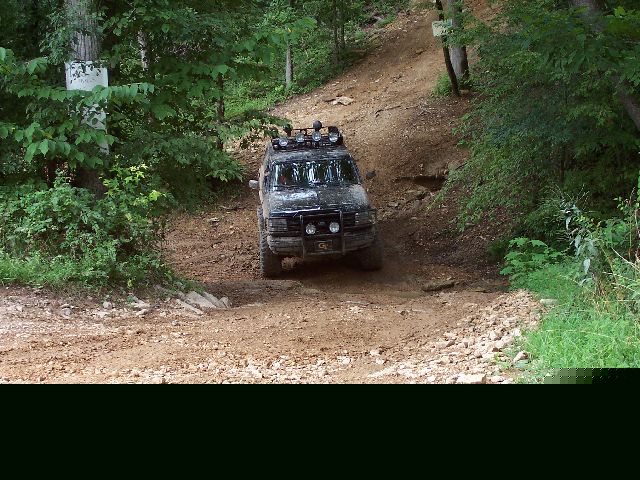 Black SUV with roof lights driving down a dirt trail in the woods