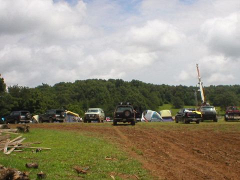 1989 Ford Bronco - A group of SUVs and tents are set up in a grassy area with a wooded backdrop.