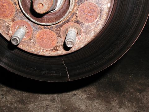 1992 Ford Taurus - Extreme close-up of a rusted brake rotor hub face with the wheel removed, showing scaled surface rust, worn wheel studs and a cracked, heat…