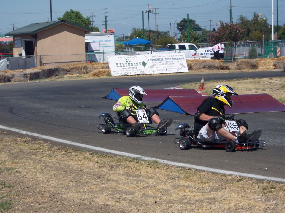 Two go-karts racing on a track, one green with number 54, the other red with number 406