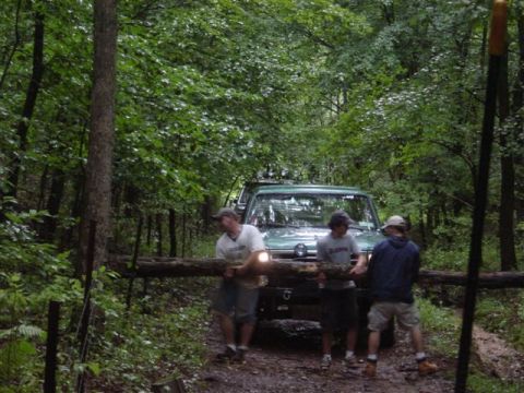 1995 Ford Bronco - Three men lift a fallen log off a muddy wooded trail in front of a green Ford Bronco with roof-mounted lights and a brush guard. The truck…