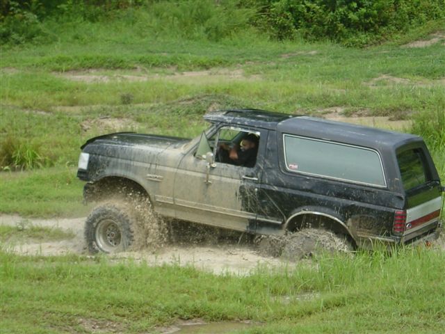 Black Ford Bronco with doors removed splashing through a muddy pit, side view