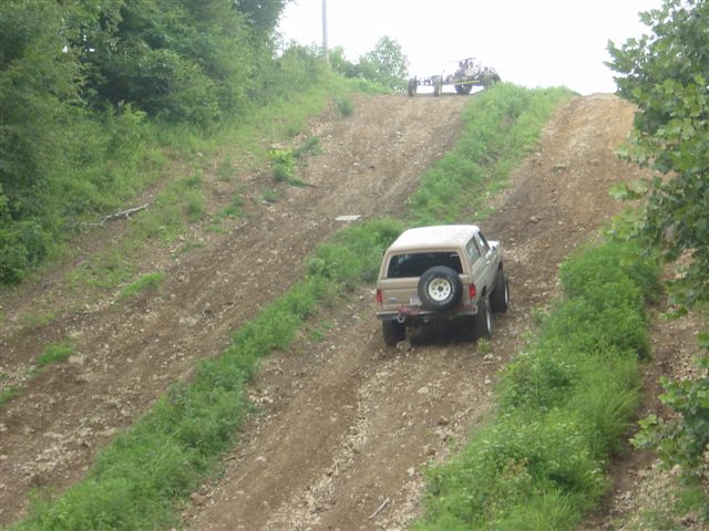 Tan Ford Bronco with rear-mounted spare tire climbing a steep dirt hill