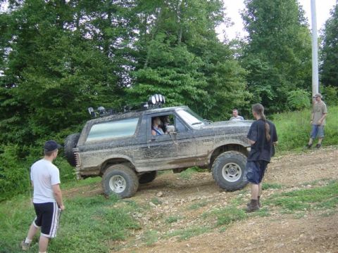 1995 Ford Bronco - Passenger-side view of a mud-caked Ford Bronco climbing a rocky dirt hill with the doors removed, a spare tire mounted on the rear quarter…