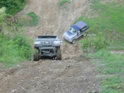 1995 Ford Bronco - Two lifted 1980s-90s Ford full-size trucks work a steep dirt hillclimb at an off-road park: one climbs nose-up toward the camera with its f…