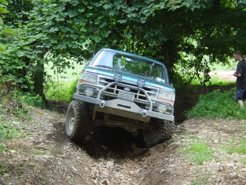 1995 Ford Bronco - A lifted teal and silver two-tone Ford Bronco flexes through a rutted dirt trail on an off-road course, front driver-side tire dropped into…