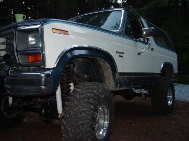 Lifted white and dark blue Ford Bronco with big mud tires and alloy wheels, front three-quarter view outdoors