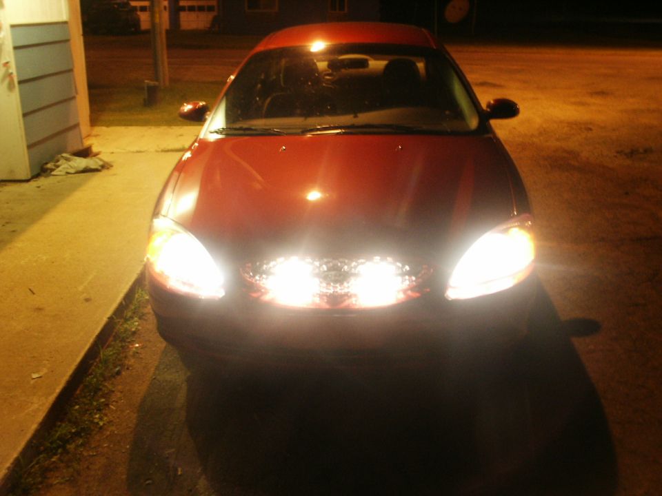 Front view of a red 2000 Ford Taurus with headlights and fog lights on