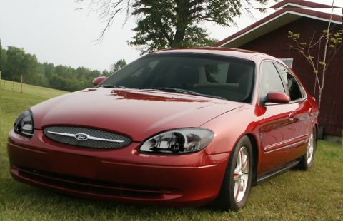 2000 Ford Taurus - This red 2000 Ford Taurus is shown from a three-quarter front angle, parked on grass in front of a building.