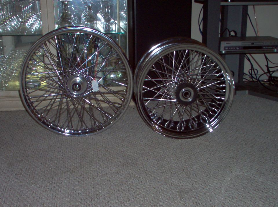 Two chrome wire wheels with many spokes, one on the left and one on the right, on a carpeted floor