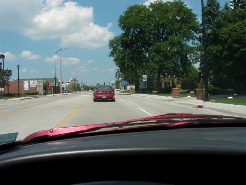 1997 Ford Taurus - Red 1997 Ford Taurus seen from behind on a road with buildings and trees.