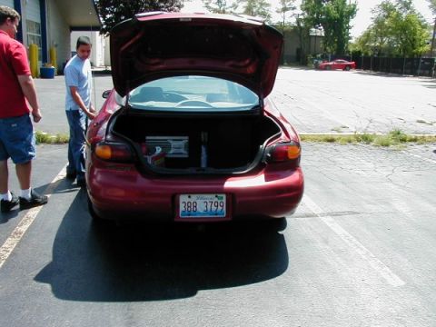 1997 Ford Taurus - A red sedan is parked with its trunk open, revealing an amplifier and other items inside.