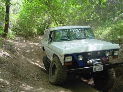 1986 Ford Bronco - This white SUV, possibly a Ford Bronco, navigates a dirt trail with its front end and winch clearly visible.