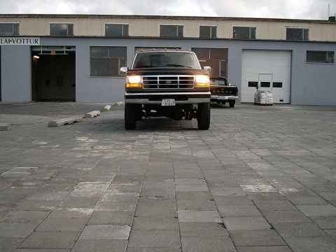 1996 Ford Bronco - A black Ford F-Series truck is parked in front of a building with a garage door.