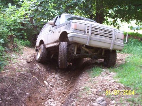 1995 Ford Bronco - This 1987 Ford Bronco is navigating a steep, muddy trail with trees on either side.
